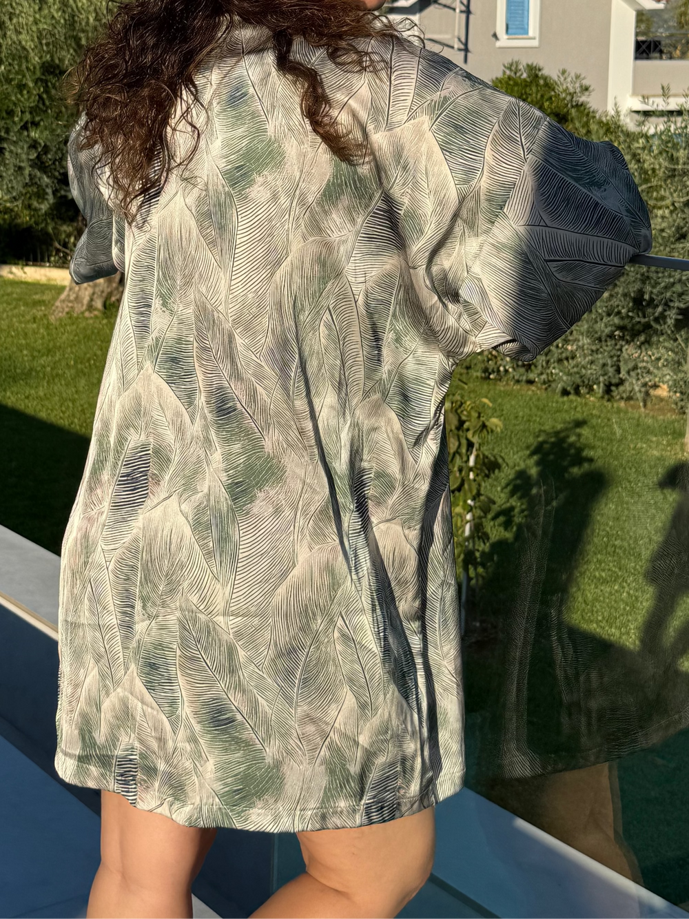 Person wearing a patterned shirt outdoors with greenery in the background