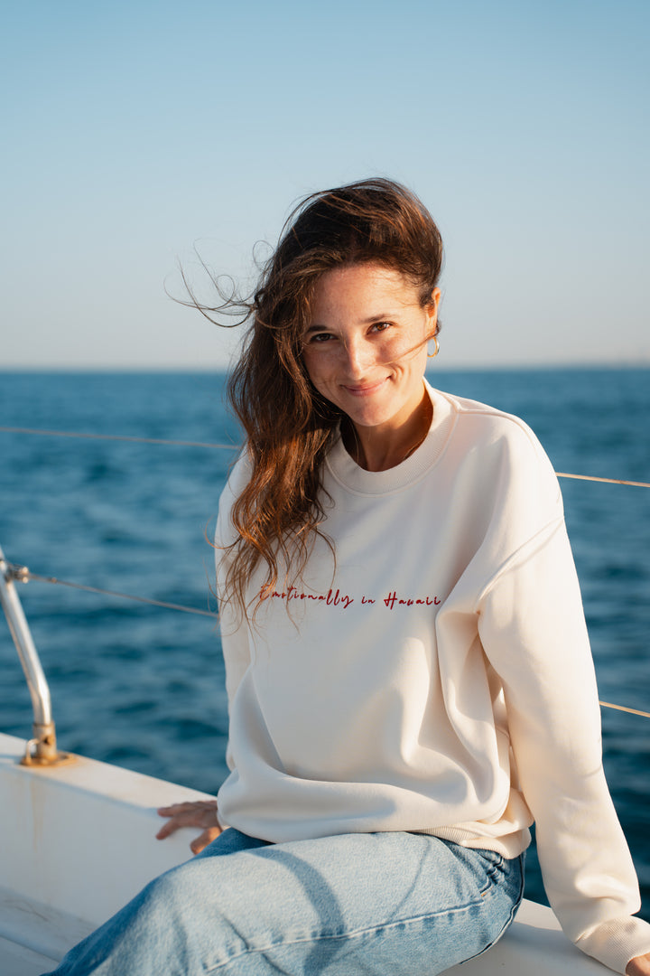 בחורה לובשת סוויטשירט לבן עם לוגו אדום קטן, עומד ליד האוקיינוס – מראה נקי, מודרני ומלא סטייל, שמשקף את הקסם והנוחות של Lika Swimwear בכל רגע על החוף והים.