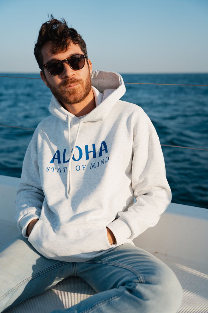 בחור לובש סוויטשירט לבן עם כיתוב Aloah , על סירה ליד האוקיינוס – מראה שמשלב חופש, נוחות וסטייל ייחודי, בדיוק כמו כל פריט מ-Lika Swimwear שמלווה אותך בכל הרגעים על הים והחוף.