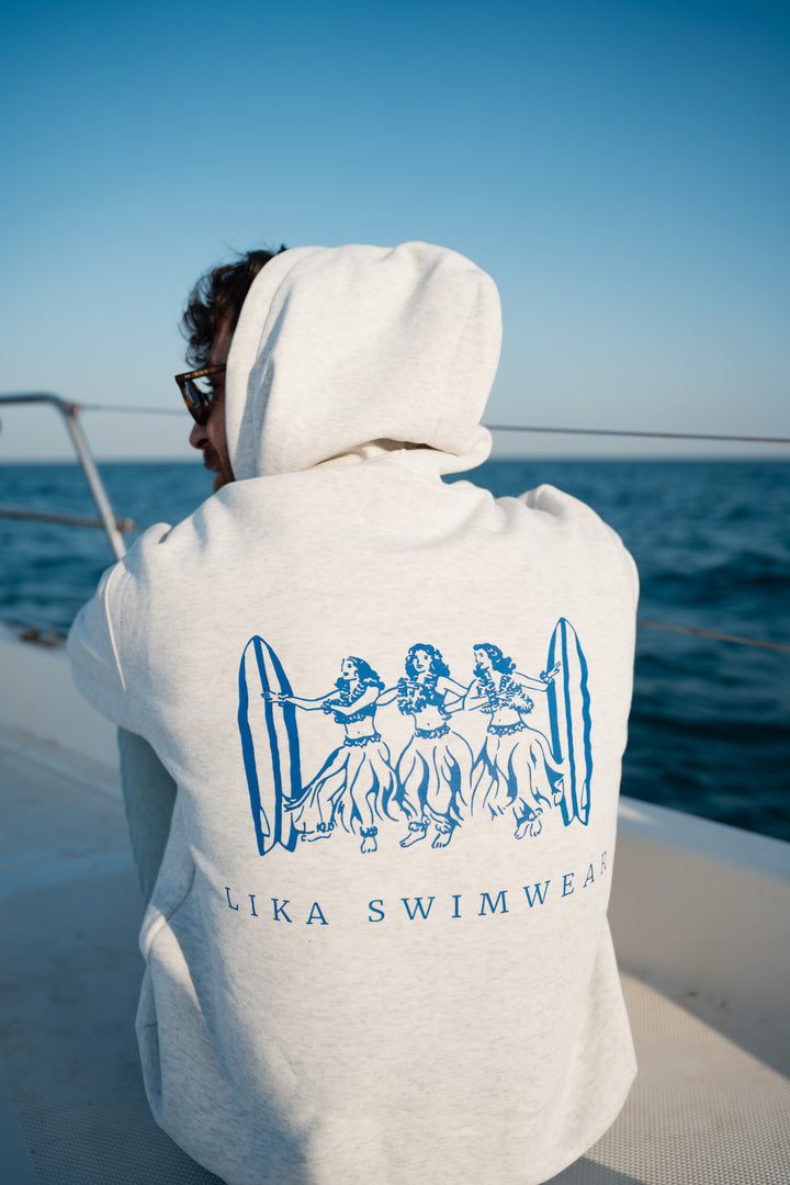 בחור לובש סוויטשירט לבן עם לוגו 'Lika Swimwear', על סירה ליד האוקיינוס – מראה שמשלב חופש, נוחות וסטייל ייחודי, בדיוק כמו כל פריט מ-Lika Swimwear שמלווה אותך בכל הרגעים על הים והחוף.