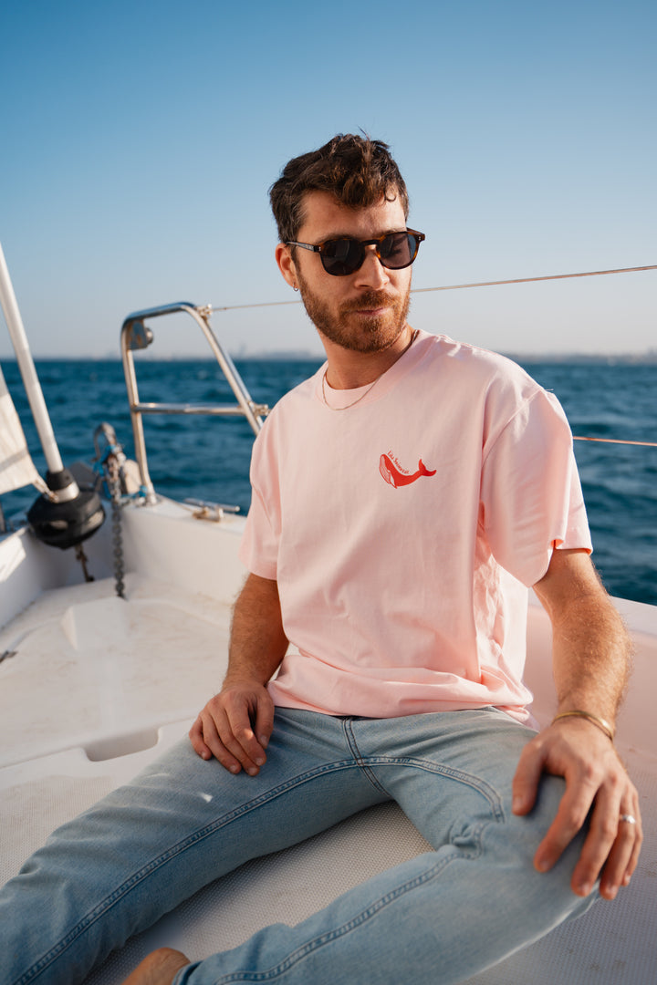 גבר לובש טי-שירט לבנה עם לוגו, מביט אל המים – מראה שמשדר רוגע, ביטחון וסטייל נקי, כמו כל פריט ב-Lika Swimwear שמבטיח נוחות וייחודיות בכל הופעה, מהחוף ועד הבילוי בעיר.