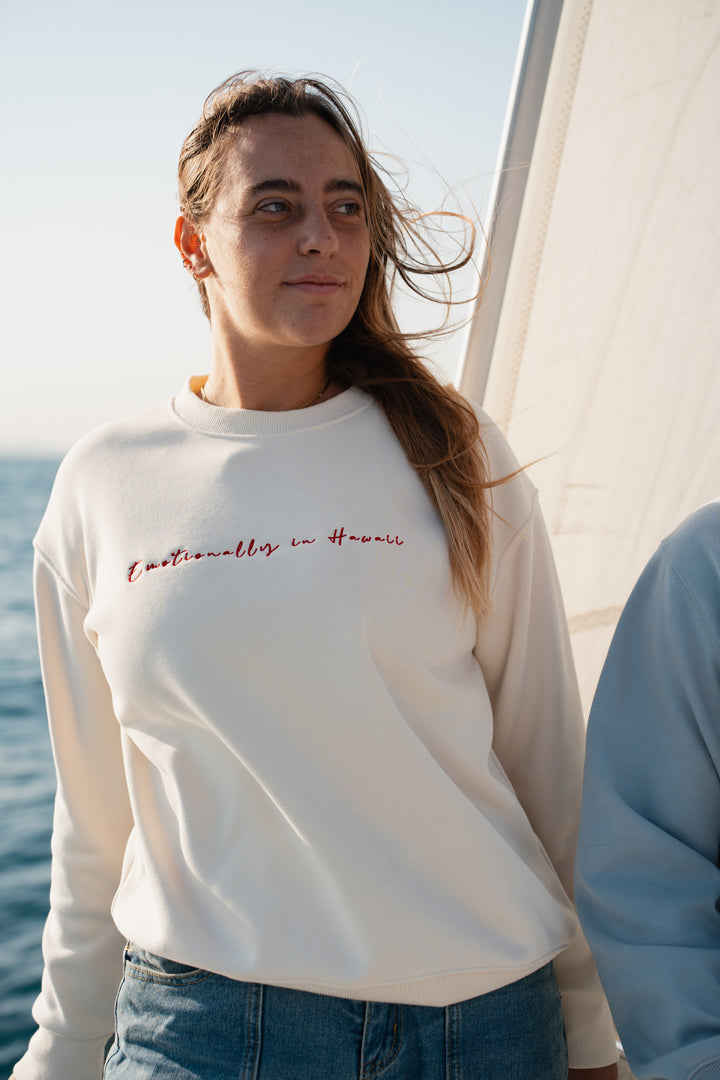 אישה על יאכטה לובשת סוויטשירט לבן עם טקסט – מראה שמשדר קלילות, חופש וסטייל ייחודי, בדיוק כמו כל פריט ב-Lika Swimwear שמלווה אותך ברגעים המיוחדים שלך על המים והחוף.