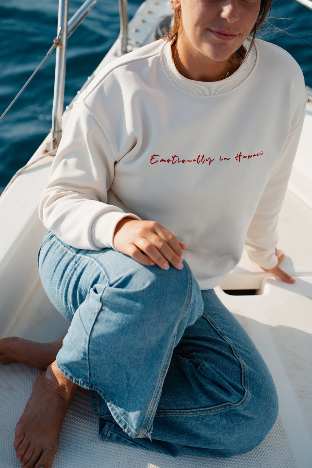 אישה על יאכטה לובשת סוויטשירט לבן עם טקסט – מראה שמשדר קלילות, חופש וסטייל ייחודי, בדיוק כמו כל פריט ב-Lika Swimwear שמלווה אותך ברגעים המיוחדים שלך על המים והחוף.