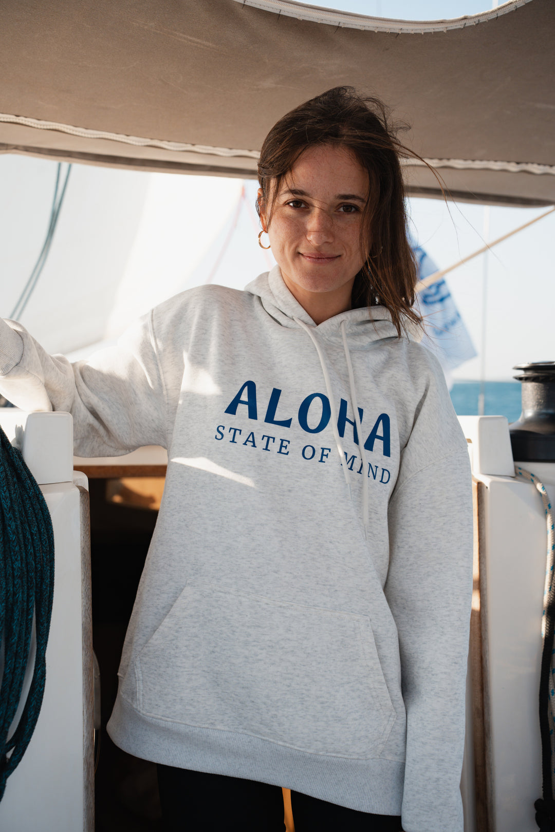 בחורה לובשת סוויטשירט אפור בהיר על סירה, עם רקע של שמיים צלולים – מראה נינוח, מודרני וסטייליסטי, בדיוק כמו כל פריט ב-Lika Swimwear שמבטיח נוחות וייחודיות בכל הרגעים שלך על המים והחוף.