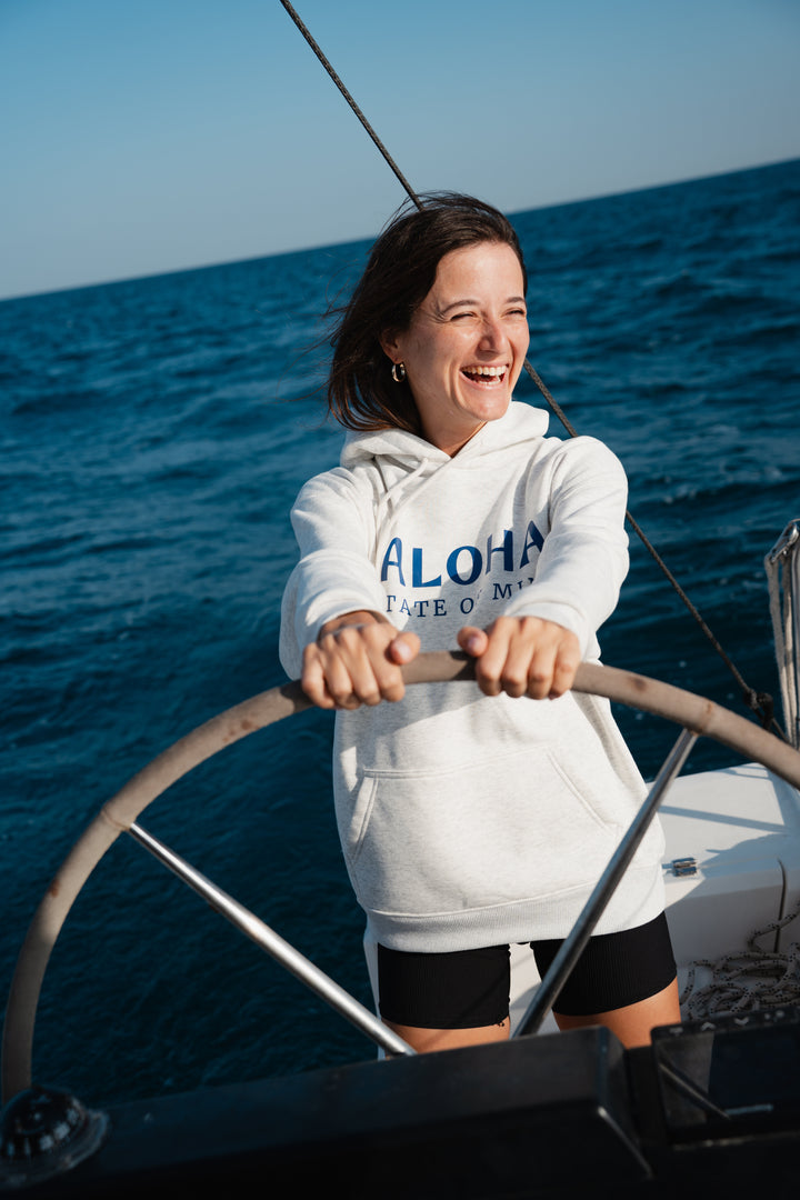 בחורה לובשת סוויטשירט אפור בהיר על סירה, עם רקע של שמיים צלולים – מראה נינוח, מודרני וסטייליסטי, בדיוק כמו כל פריט ב-Lika Swimwear שמבטיח נוחות וייחודיות בכל הרגעים שלך על המים והחוף.