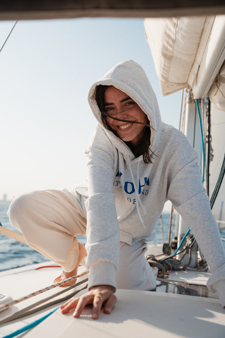 בחורה לובשת סוויטשירט אפור בהיר על סירה, עם רקע של שמיים צלולים – מראה נינוח, מודרני וסטייליסטי, בדיוק כמו כל פריט ב-Lika Swimwear שמבטיח נוחות וייחודיות בכל הרגעים שלך על המים והחוף.